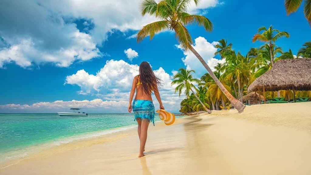 Woman on a tropical beach under a palm tree looking at the sea.