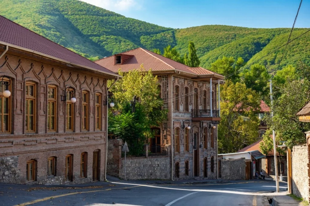 A charming street view in the historic center of Sheki, Azerbaijan, featuring traditional brick buildings against a backdrop of green mountains.