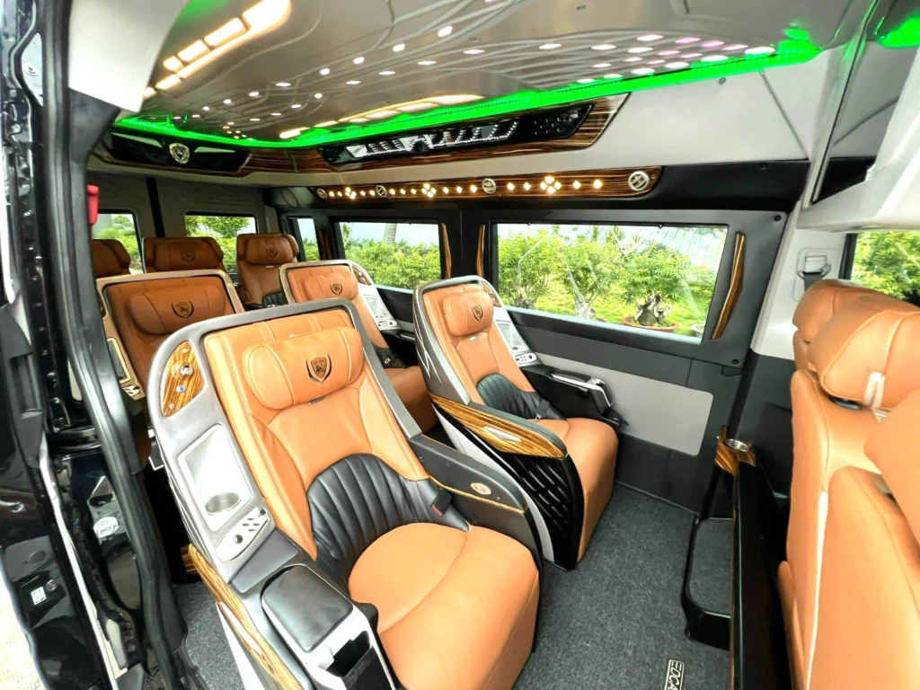 The luxurious interior of a VIP transport van, featuring premium tan and black leather reclining seats, wood grain accents, and ambient green ceiling lighting.