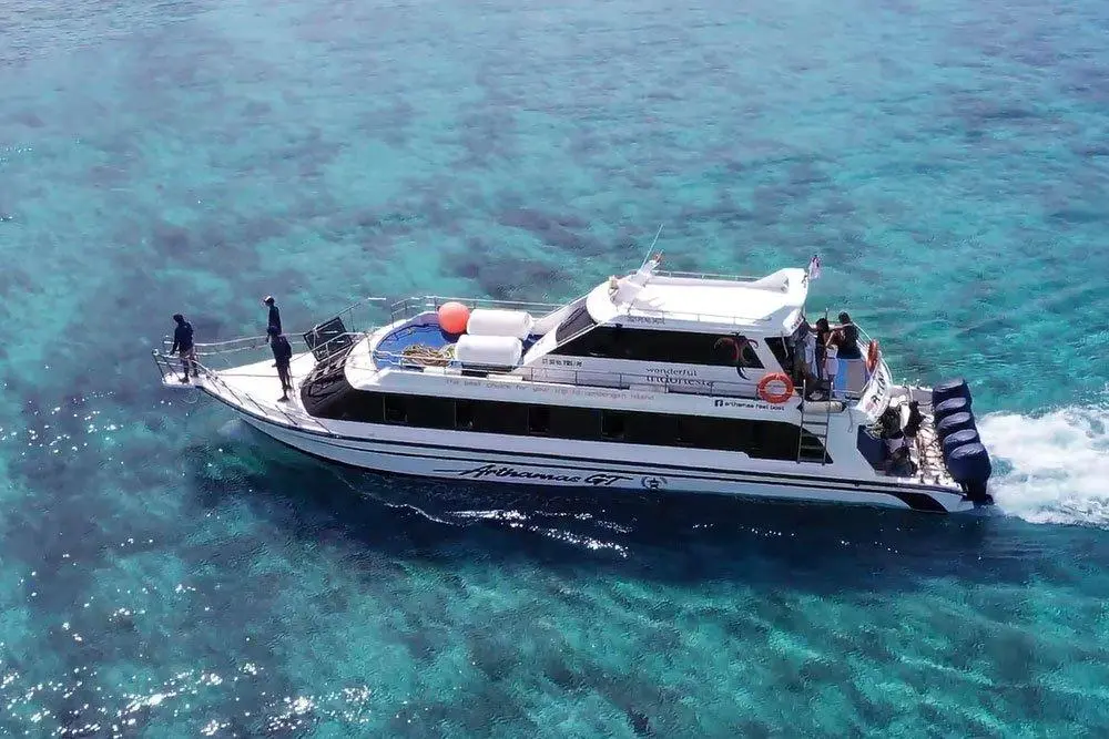 An aerial view of the white Arthamas Express speedboat cruising at high speed over clear, turquoise, shallow coral reef waters.