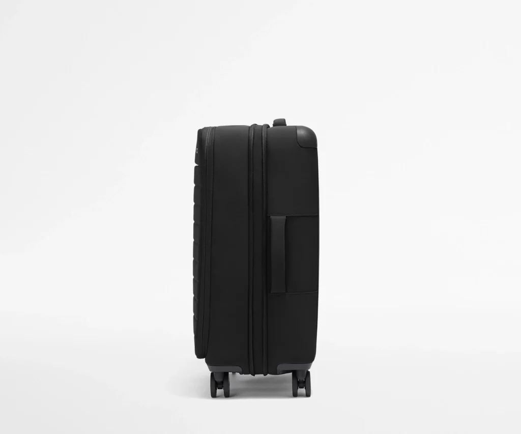 Side profile of a premium matte black hard-shell suitcase standing upright on wheels against a clean white background.