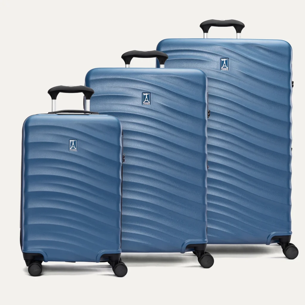 A smiling woman in an all-white outfit walking with a blue hard-shell carry-on suitcase against a plain white background.