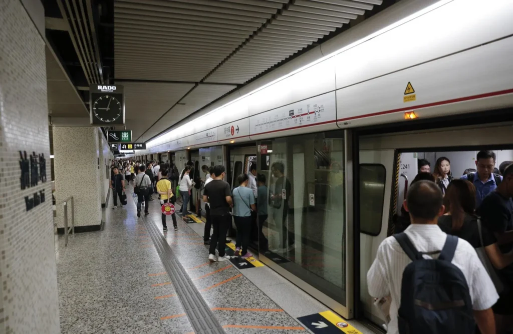 Interior view of the Sheung Wan MTR station platform in Hong Kong with digital train arrival signs, platform screen doors, and an escalator.
