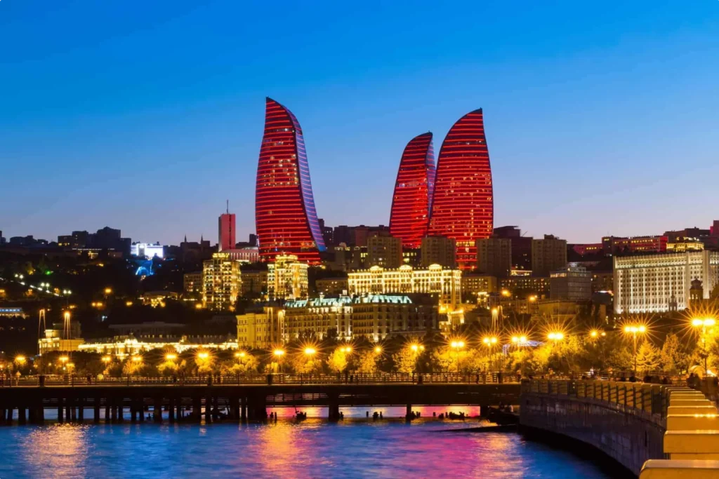 The iconic Flame Towers in Baku, Azerbaijan, illuminated in vibrant red light against a deep blue twilight sky, overlooking the city and waterfront.