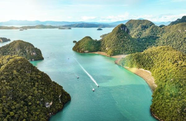 An aerial landscape view of the lush green coastline of Langkawi, featuring a small marina, turquoise waters, and distant islands under a blue sky.
