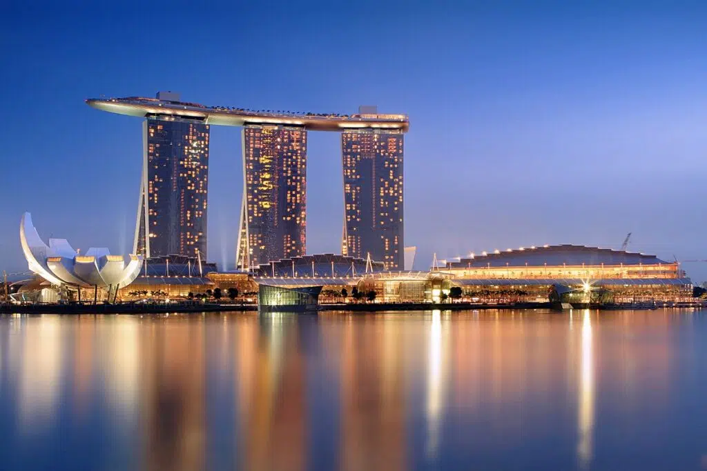 The iconic Marina Bay Sands hotel in Singapore with its signature rooftop skypark, illuminated at twilight across the calm waters of the bay.