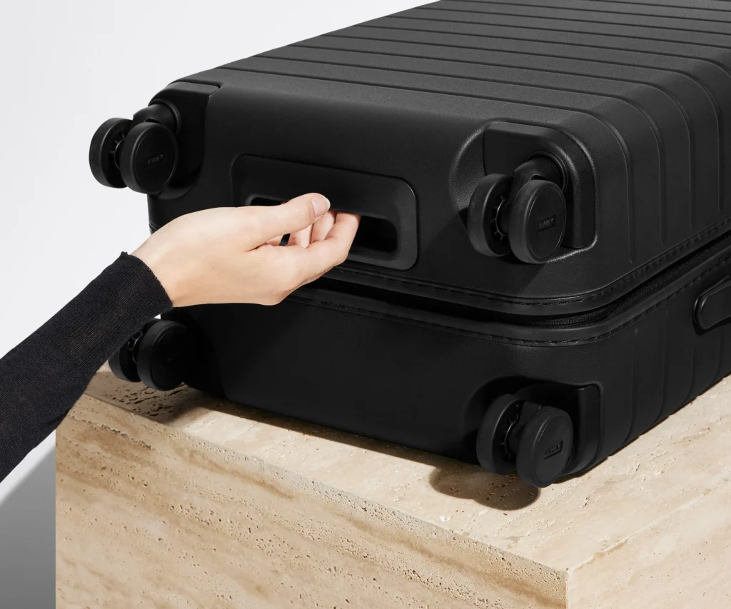 Side profile of a premium matte black hard-shell suitcase standing upright on wheels against a clean white background.