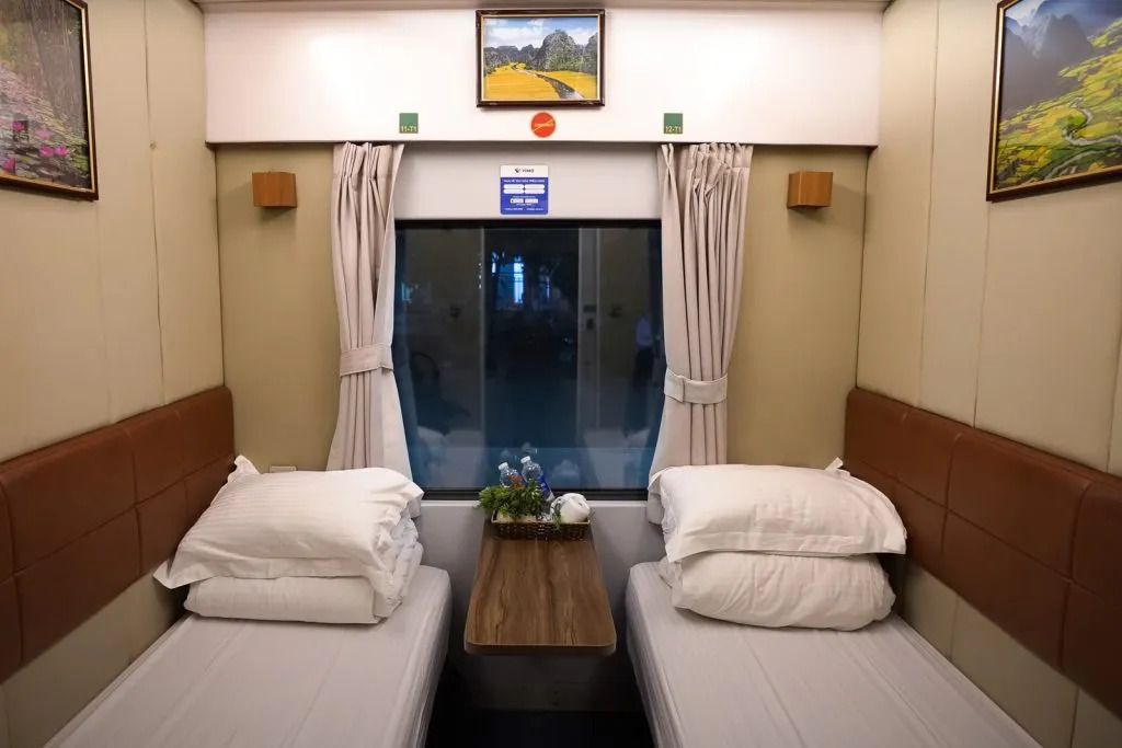 The cozy interior of a sleeper train compartment featuring comfortable bunk beds with plush bedding, privacy curtains, and soft reading lights.