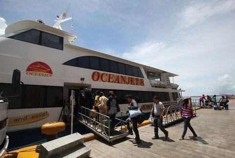 Passengers walk up a ramp to board the white OceanJet 8 ferry at a concrete pier on a sunny day with a blue sky overhead.