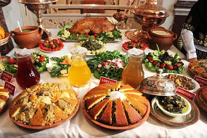 A table laden with traditional Azerbaijani dishes, including various types of plov, freshly baked bread, colorful vegetable salads, and clay pots.