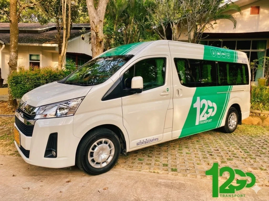 A white 12Go Transport branded minivan parked outdoors, showcasing its green and white livery used for passenger transportation services.