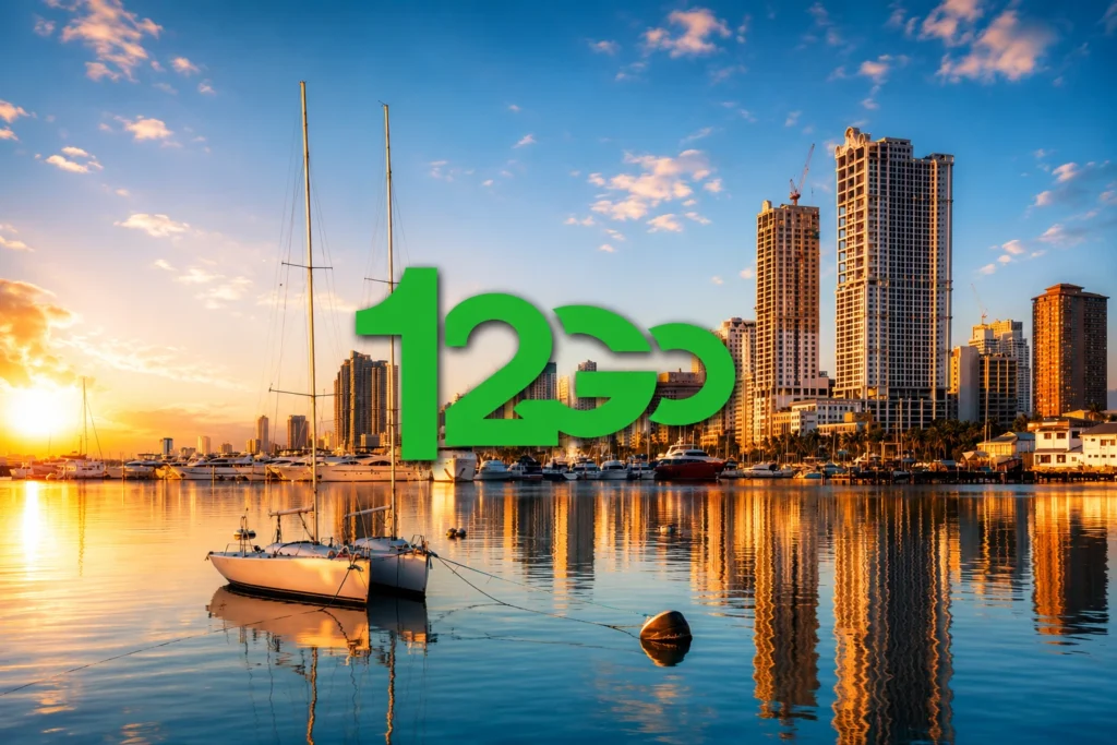 A large green 12Go logo centered over a calm marina with sailboats, yachts, and city skyscrapers reflecting in the water during a golden sunset.
