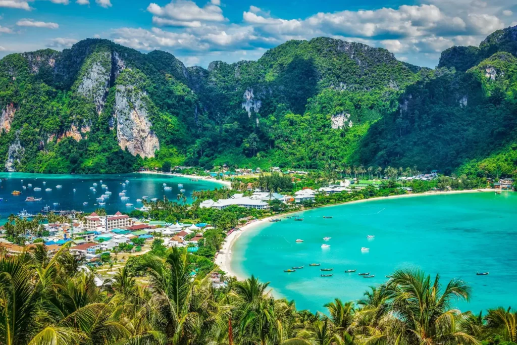 A stunning high-angle view of Phi Phi Islands in Thailand, showing a sandy beach, turquoise waters, and lush green mountains under a bright sky.