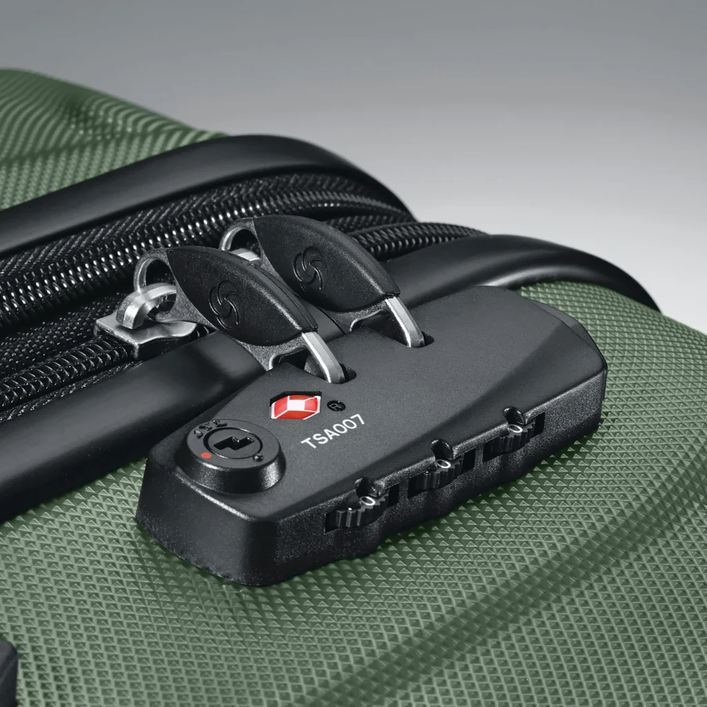 A close-up of a black TSA-approved combination lock secured on a textured green suitcase, showing the locking mechanism and zipper pulls.