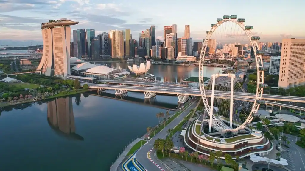 A stunning nighttime view of the Singapore Flyer, a giant observation wheel, illuminated with vibrant lights against the city skyline and Marina Bay waterfront.