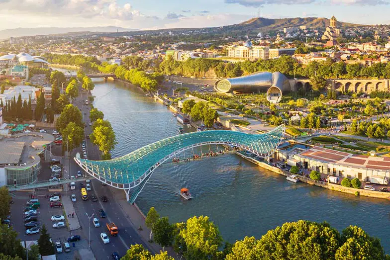 A scenic view of the Kura River flowing through Tbilisi, Georgia, reflecting the historic buildings and modern architecture along its banks.