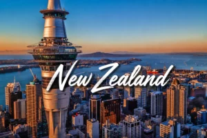 Aerial view of the iconic Sky Tower standing tall over the Auckland city skyline, with the harbor and distant islands visible during sunset.