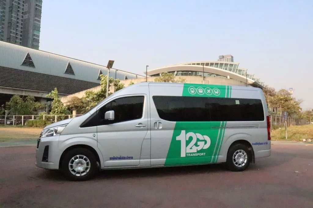 A silver 12Go Transport minivan with green branding parked outside a modern building.