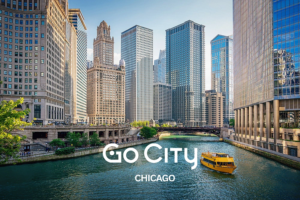 A yellow tour boat travels down the Chicago River, surrounded by the city's iconic skyscrapers with the Go City Chicago logo displayed.