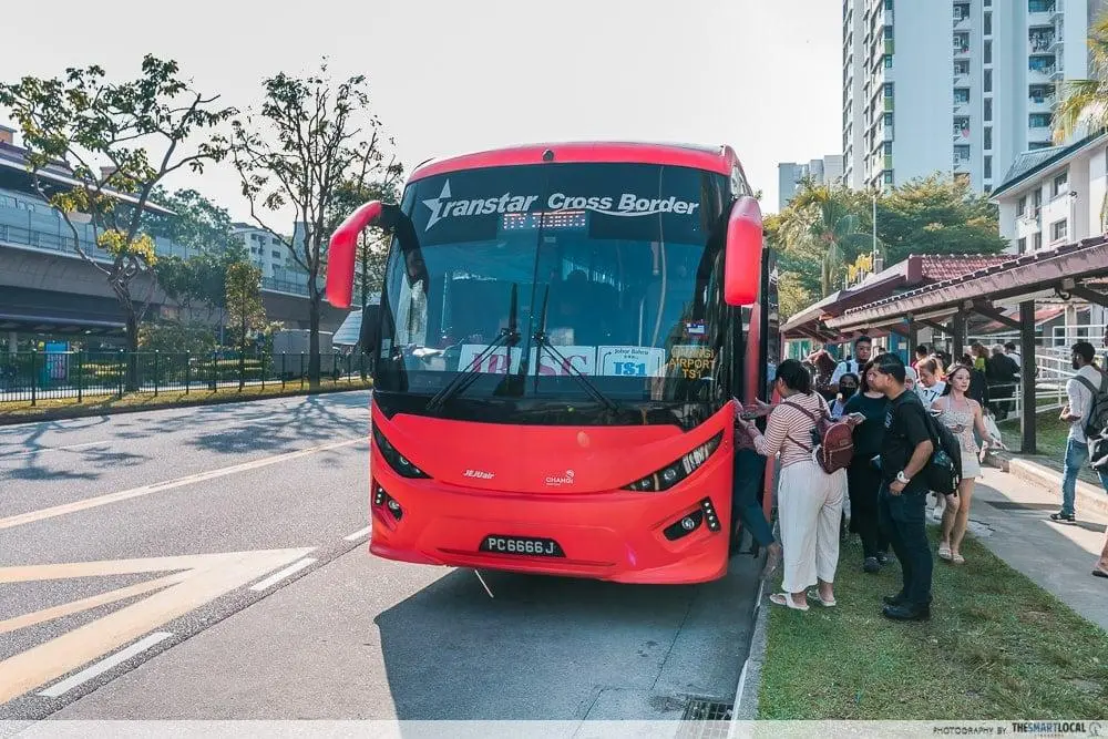 Passengers boarding a bright red Transtar Cross Border bus at a designated stop during the day.