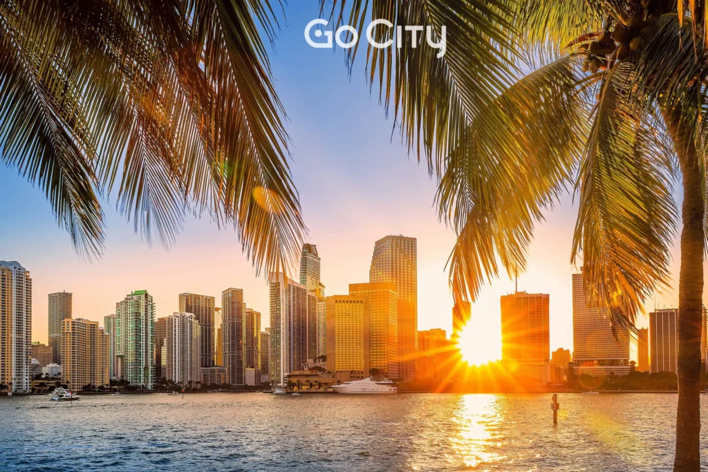 The Miami skyline at sunset framed by palm tree fronds in the foreground, with the Go City logo centered at the top.