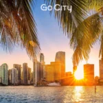 The Miami skyline at sunset framed by palm tree fronds in the foreground, with the Go City logo centered at the top.