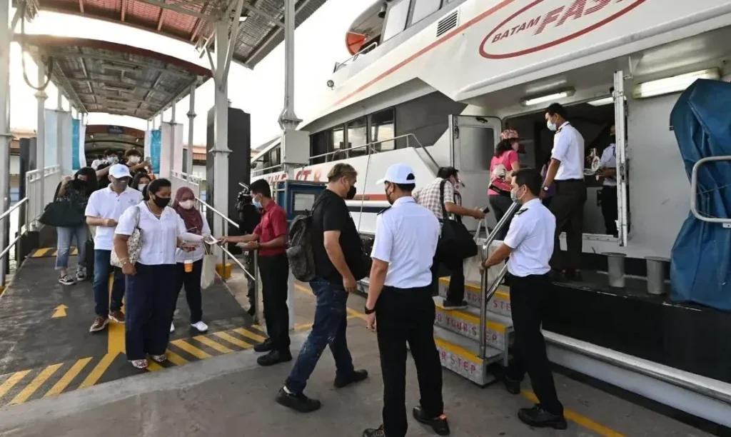 assengers boarding a Batam Fast ferry from a terminal walkway, assisted by crew members at the entrance.