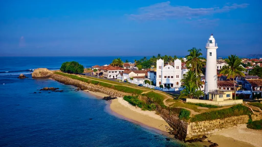 Aerial view of the historic Galle Lighthouse and fort ramparts along the scenic coastline and blue ocean in Sri Lanka.