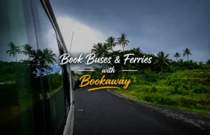 View from inside a moving vehicle driving along a lush tropical road with palm trees, featuring overlaid text that reads "Book Buses & Ferries with Bookaway".