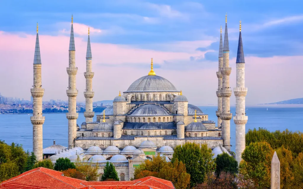 The majestic Blue Mosque in Istanbul featuring multiple cascading domes and tall minarets against a blue sky with the sea in the background