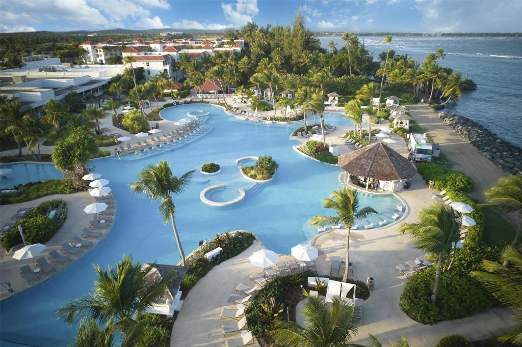 Aerial view of Hyatt Regency Grand Reserve Puerto Rico showcasing its large swimming pool, red-tiled resort buildings, palm trees, and coastal background