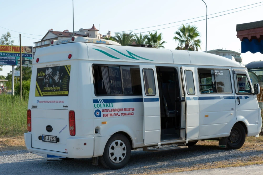 A white public transport minibus or dolmus parked with its side door open, operating in Turkey