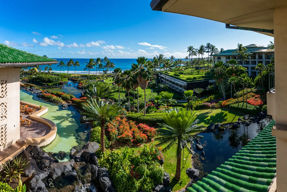 Aerial view of the Grand Hyatt Kauai Resort & Spa swimming pool surrounded by palm trees and cabanas, leading out to a tropical white sand beach and turquoise sea.