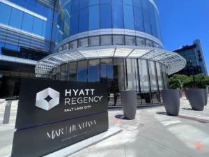 Exterior view of the modern glass facade at Hyatt Regency Salt Lake City featuring the entrance sign and Mar | Muntanya restaurant branding.