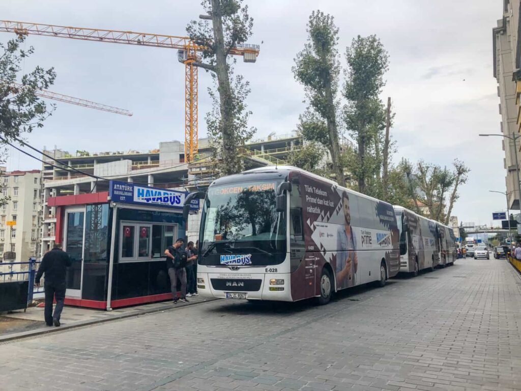 A Havabus airport shuttle bus parked at a station stop on a cobblestone street in Istanbul next to a ticket booth