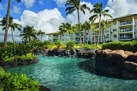 A pristine lagoon-style swimming pool surrounded by volcanic rock formations, lush greenery, and towering palm trees at Grand Hyatt Kauai.