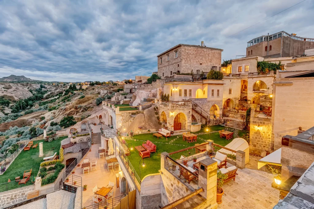 An elevated view of a luxury cave hotel in Cappadocia featuring lit terraces, outdoor seating areas, and stone architecture at dusk