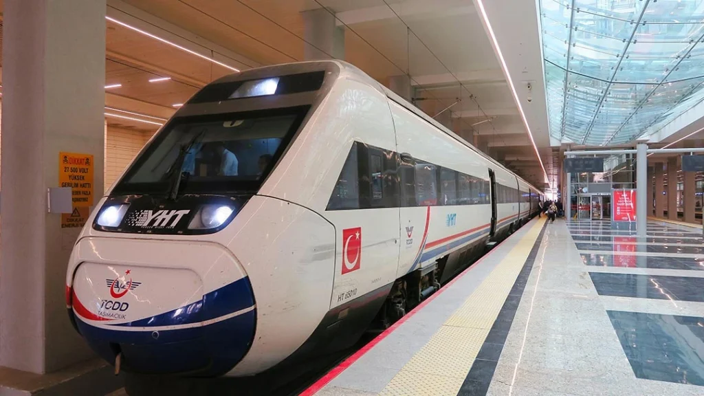 A modern TCDD YHT high-speed passenger train parked at a platform inside a bright, contemporary train station