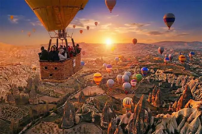 Passengers in a hot air basket enjoying a sunrise flight over the unique rock formations and landscape of Cappadocia dotted with colorful balloons