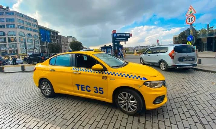 A yellow taxi cab parked on a paved street in Istanbul with city buildings and a traffic sign in the background