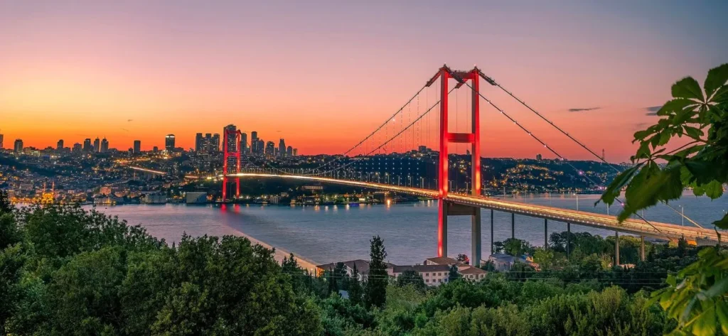 The illuminated Bosphorus Bridge spanning the water in Istanbul during a vibrant sunset with the city skyline in the background.