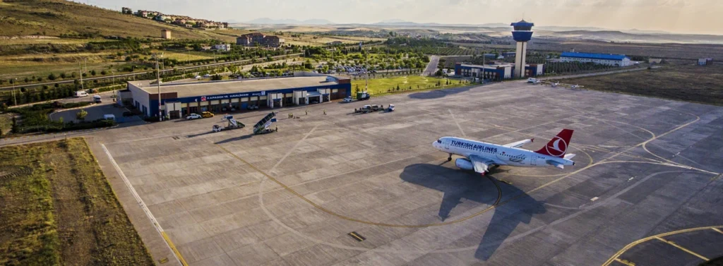 Aerial view of Nevşehir Kapadokya Airport in Turkey with a parked passenger airplane on the tarmac and terminal buildings.