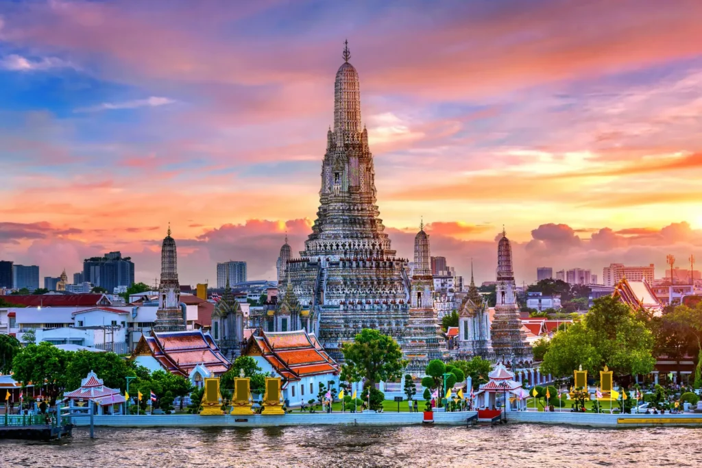 View of the magnificent Wat Arun temple in Bangkok, Thailand, illuminated by a vibrant sunset sky over the river.