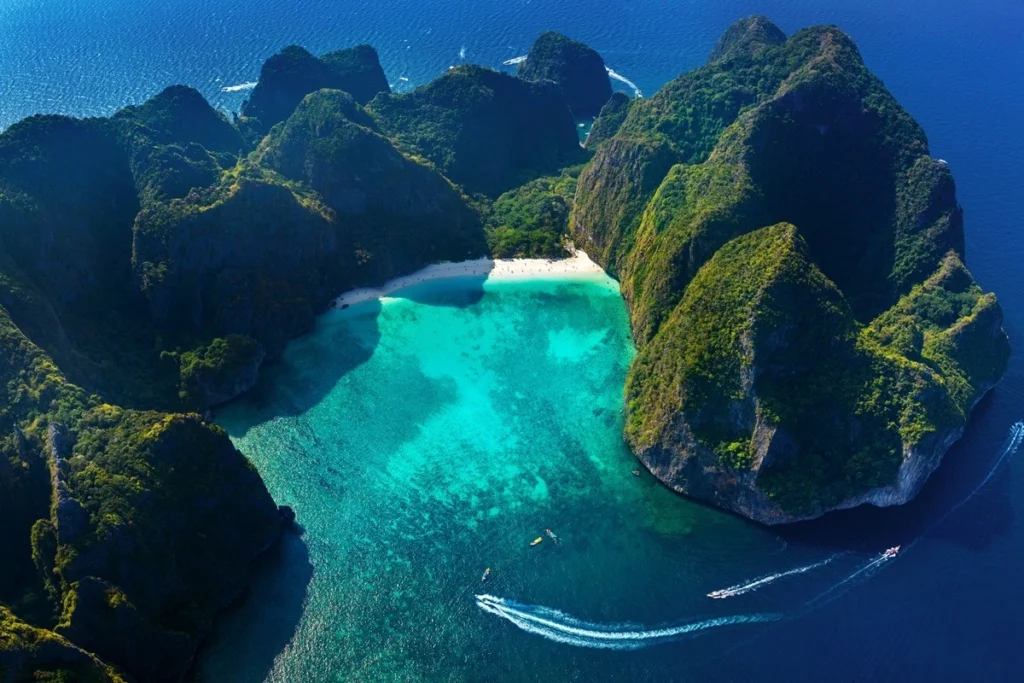 Aerial view of Maya Bay in Thailand, showing its hidden white sand beach surrounded by dramatic limestone cliffs and turquoise water.