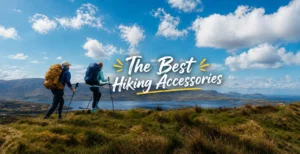 Two hikers with backpacks and trekking poles walking along a grassy ridge overlooking a lake and distant mountain ranges