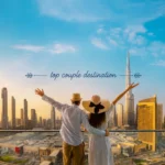 A couple standing with arms raised on a balcony overlooking the modern Dubai city skyline and Burj Khalifa.