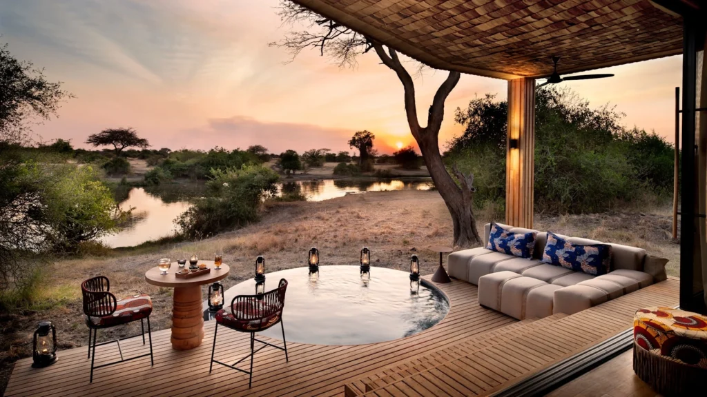 A luxury safari lodge wooden deck featuring a plunge pool, seating area, and scenic views of a river at sunset