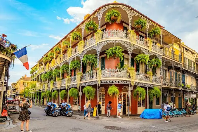 A historic brick building in New Orleans featuring multi-level wrought iron balconies adorned with lush hanging ferns and plants