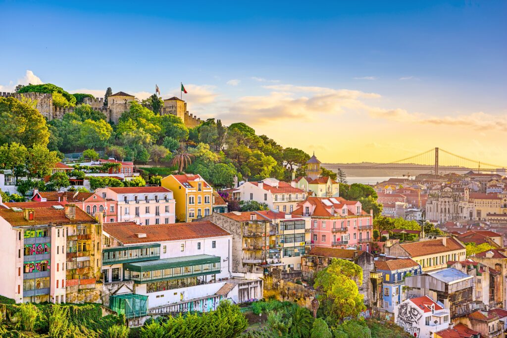 Panoramic view of Lisbon, Portugal, featuring historic colorful buildings, a hilltop castle, and a suspension bridge in the background
